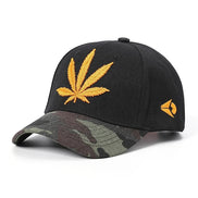 AKJ Fashion black baseball cap with adjustable strap, featuring a yellow embroidered cannabis leaf and camouflage brim.