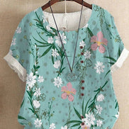 AKJ Fashion blouse effet lin vert à fleurs de glycines violettes et papillons, boutonnage décalé, manches courtes roulottées.