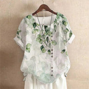 AKJ Fashion blouse blanche à imprimé feuilles vertes, col rond, manches courtes retroussées, boutonnage décalé.