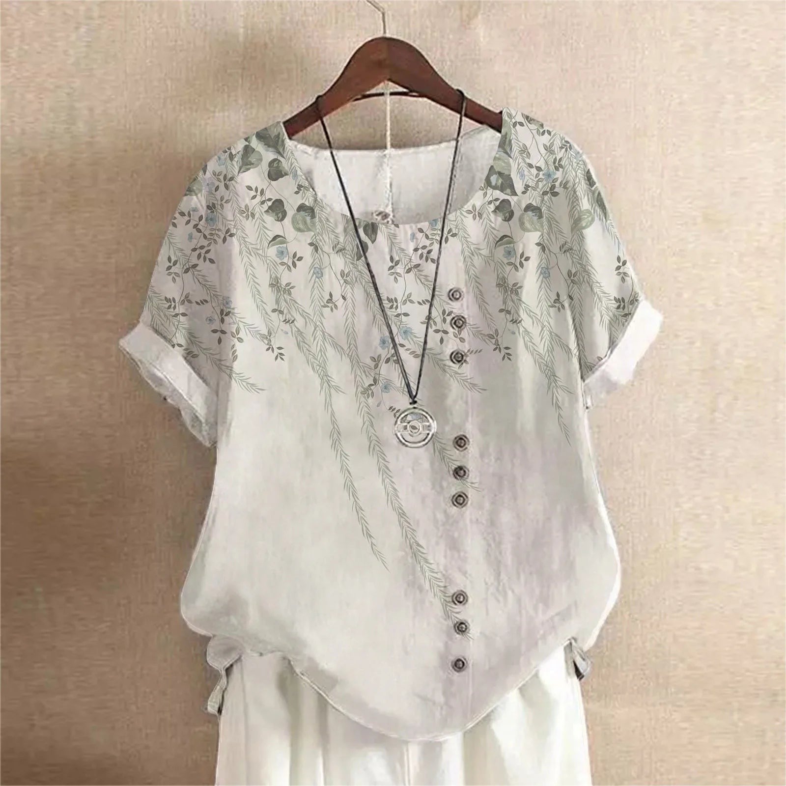 AKJ Fashion blouse blanche à imprimé floral violet et feuilles vertes, col rond, manches courtes retroussées, boutonnage décalé.