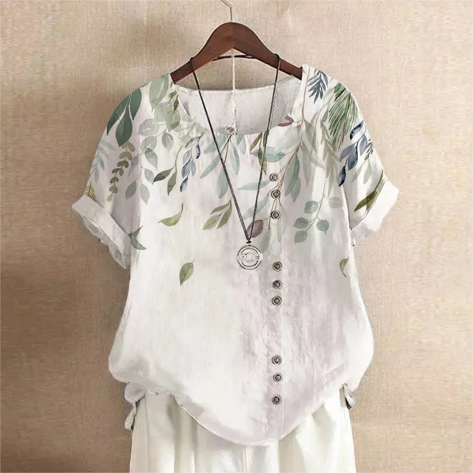 AKJ Fashion blouse blanche à imprimé feuilles vertes et violettes, col rond, manches courtes retroussées, boutonnage décalé.