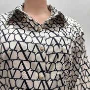 Chemise AKJ Fashion en satin écru et noir, col pointu, boutons dorés, imprimé graphique, coupe droite.