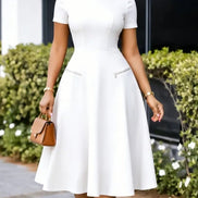 AKJ Fashion robe midi blanche évasée à manches courtes, col rond et poches zippées décoratives. Coupe ajustée.
