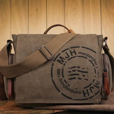 Sac bandoulière AKJ Fashion en toile vintage kaki, avec logo rond noir et bandoulière réglable.